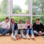 Leute sitzen am Boden und schauen zusammen in eine Laptop