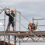 Zwei Gerüstbauer beim Aufbauen eines Gerüstes auf einem Dach